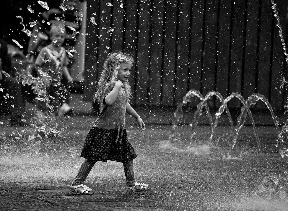 A Little girl plays in the fountain in the city 