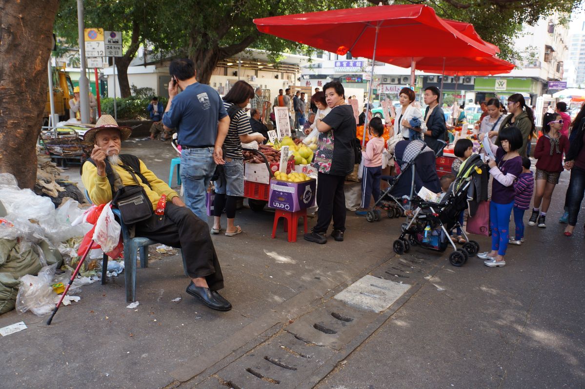 Een typische chinese oude man op een pleintje in Yuen Long waar ook fruit en groente verkocht wordt. Er is zoveel gaande op deze foto: de man, de mensen, de markt, de omgeving en vooral de cultuur die ervan af spat. 