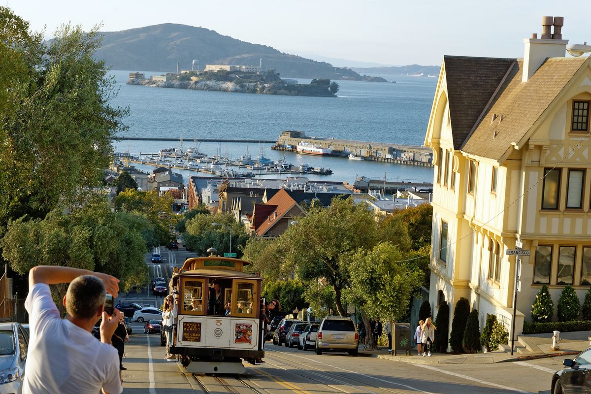 Die Cable Cars sind bei Touristen ein beliebtes Verkehrsmittel und ein Erkennungszeichen dafür dass man sich in San Francisco befindet. In Hintergrund ist die Bucht von San Francisco mit dem ehemaligem Gefängnis Alcatraz zuerkennen. Location : San Francisco in US-Bundesstaat Kalifornien in Jahr 2015