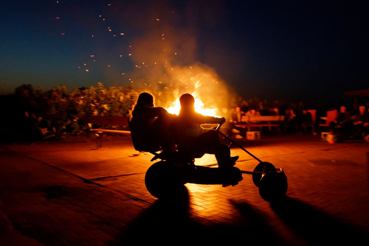 Kinder umrunden mit einen "Kettcar" ein Osterfeuer