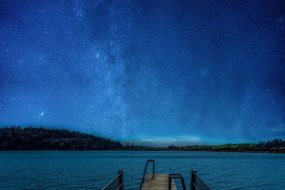 Mindelsee auf dem Bodanrück am 05.03.23 um 21:36 Uhr. Licht Zusammenspiel von aufgehendem Vollmond und Sternenhimmel, links über den Waldwipfeln ist die Andromeda Galaxie zu sehen.